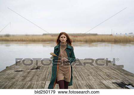 Stock Photo - Serious Caucasian woman walking on dock holding stalk of grass. Fotosearch