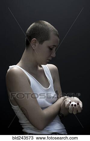 Stock Image - Serious Caucasian woman with shaved-head holding pills. Fotosearch