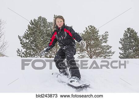 Stock Image - Serious girl riding snowboard on hill in winter. Fotosearch