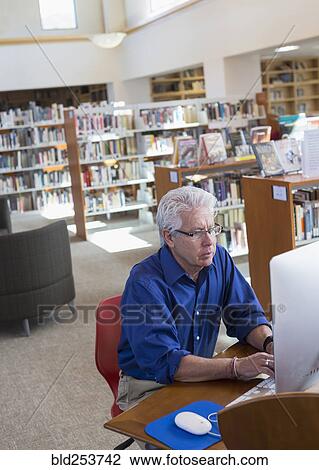 Stock Image - Serious Hispanic man using computer in library. Fotosearch
