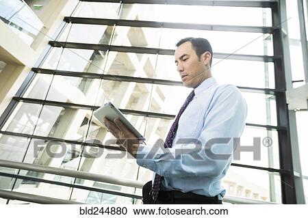Stock Image - Serious Mixed Race businessmen using digital tablet in lobby. Fotosearch