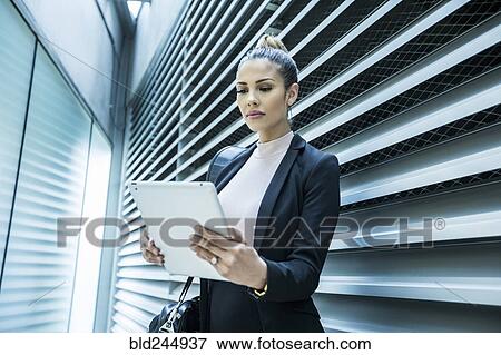 Serious Mixed Race businesswoman using digital tablet in corridor View Large Photo Image Stock Photo - Serious Mixed Race businesswoman using digital tablet in corridor. Fotosearch