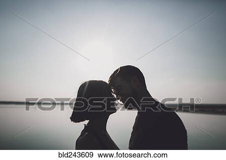 Stock Photo - Silhouette of Caucasian couple face to face at lake. Fotosearch