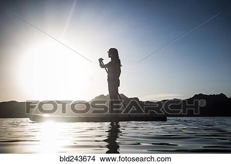 Silhouette of Caucasian woman standing on paddleboard in river View Large Photo Image Picture - Silhouette of Caucasian woman standing on paddleboard in river. Fotosearch