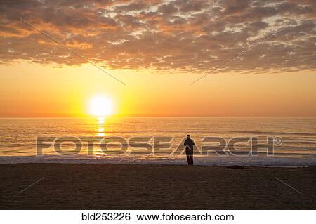 Silhouette of man standing on ocean beach at sunset View Large Photo Image Stock Photograph - Silhouette of man standing on ocean beach at sunset. Fotosearch