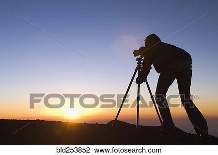 Stock Image - Silhouette of Mixed Race photographer with camera at sunset. Fotosearch