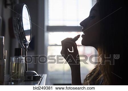 Stock Image - Silhouette of woman applying lipstick in mirror. Fotosearch