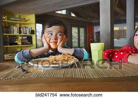 Picture - Sister watching Mixed Race brother with messy face eating spaghetti. Fotosearch