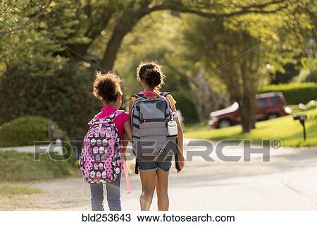 Stock Image - Sisters walking in street wearing backpacks. Fotosearch
