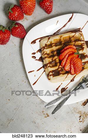 Stock Image - Sliced strawberries and chocolate syrup on waffle. Fotosearch