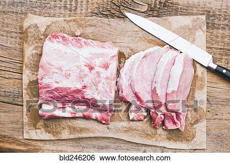Stock Photograph - Slices of raw meat on butcher paper near knife. Fotosearch