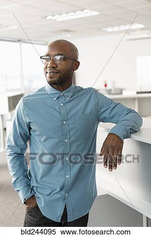 Stock Photography - Smiling African American man leaning in office. Fotosearch