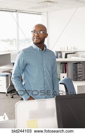 Stock Image - Smiling African American man standing in office. Fotosearch