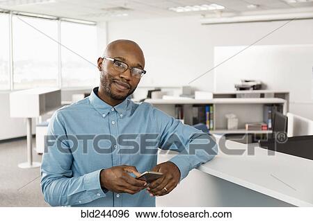 Smiling African American man texting on cell phone in office View Large Photo Image Stock Photograph - Smiling African American man texting on cell phone in office. Fotosearch