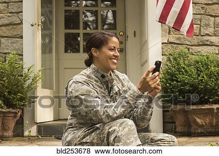 Stock Photo - Smiling African American soldier sitting on front stoop texting on cell phone. Fotosearch