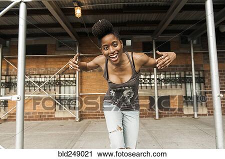 Stock Image - Smiling African American woman dancing under scaffolding. Fotosearch