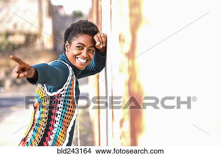 Picture - Smiling African American woman leaning on wall and pointing finger. Fotosearch