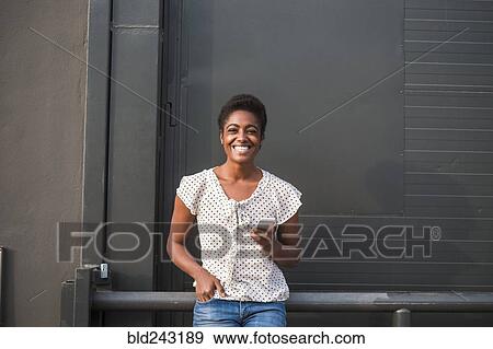 Stock Photo - Smiling African American woman leaning on railing texting on cell phone. Fotosearch