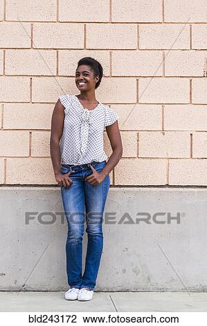 Stock Image - Smiling African American woman posing near concrete wall. Fotosearch