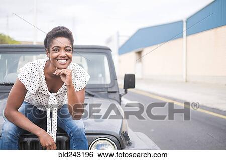 Smiling African American woman sitting on hood of car View Large Photo Image Stock Photograph - Smiling African American woman sitting on hood of car. Fotosearch