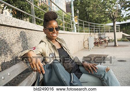 Smiling African American woman sitting on bench at park View Large Photo Image Stock Photograph - Smiling African American woman sitting on bench at park. Fotosearch