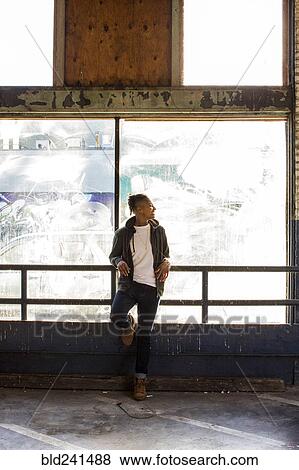 Stock Photo - Smiling androgynous Mixed Race woman leaning on railing near window. Fotosearch