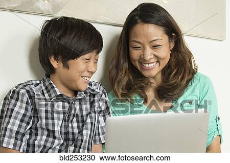 Stock Image - Smiling Asian mother and son using laptop. Fotosearch