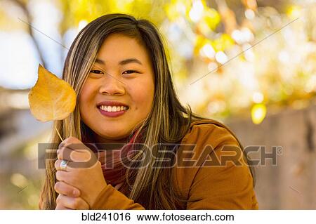 Stock Photograph - Smiling Asian woman holding leaf in autumn. Fotosearch