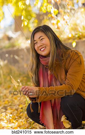 Stock Photography - Smiling Asian woman holding leaf in autumn. Fotosearch