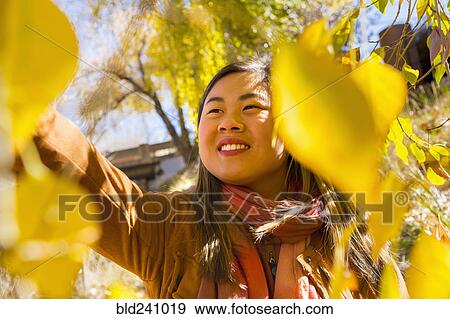 Stock Photo - Smiling Asian woman reaching for leaf in autumn. Fotosearch