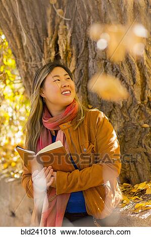 Smiling Asian woman reading book in autumn View Large Photo Image Stock Photo - Smiling Asian woman reading book in autumn. Fotosearch