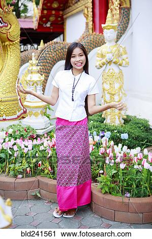 Stock Image - Smiling Asian woman standing in ornate garden. Fotosearch
