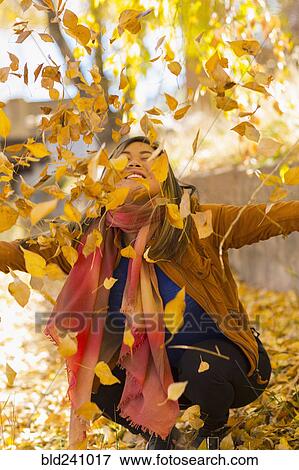 Stock Photo - Smiling Asian woman throwing leaves in autumn. Fotosearch