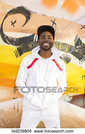 Picture - Smiling Black man leaning on graffiti wall. Fotosearch