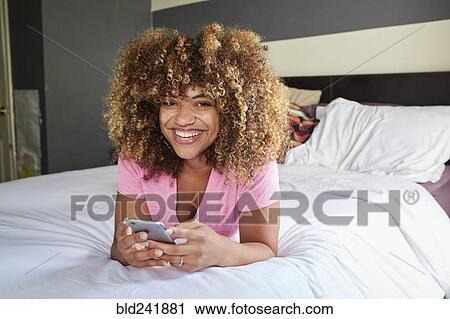 Smiling Black woman laying on bed texting on cell phone View Large Photo Image Stock Image - Smiling Black woman laying on bed texting on cell phone. Fotosearch