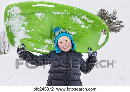 Stock Image - Smiling boy posing with toboggan in winter. Fotosearch