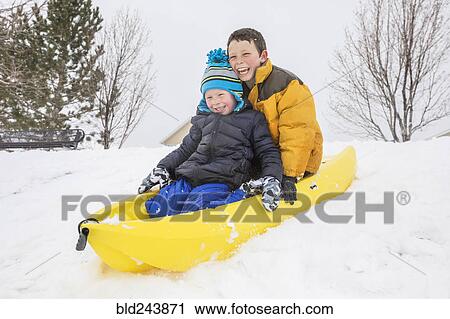 Stock Image - Smiling boys sliding on toboggan on hill in winter. Fotosearch