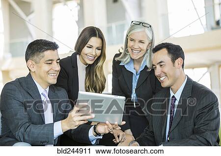 Stock Image - Smiling business people reading digital tablet in lobby. Fotosearch