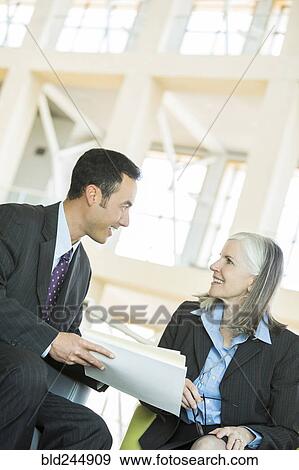 Smiling business people reading paperwork in lobby View Large Photo Image Stock Photo - Smiling business people reading paperwork in lobby. Fotosearch