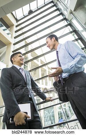 Stock Photo - Smiling businessmen talking in lobby. Fotosearch