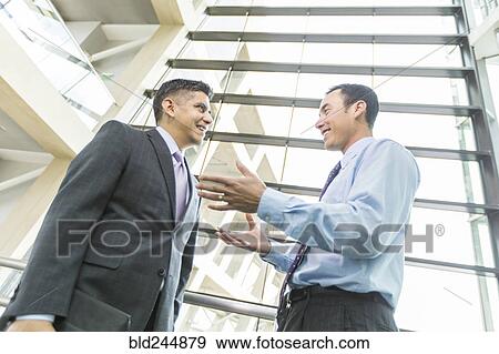 Stock Photo - Smiling businessmen talking in lobby. Fotosearch
