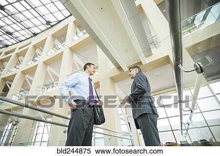 Stock Photography - Smiling businessmen talking in lobby. Fotosearch