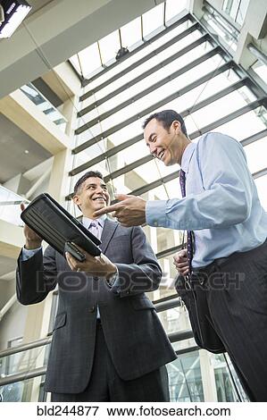 Smiling businessmen using digital tablet in lobby View Large Photo Image Stock Photo - Smiling businessmen using digital tablet in lobby. Fotosearch