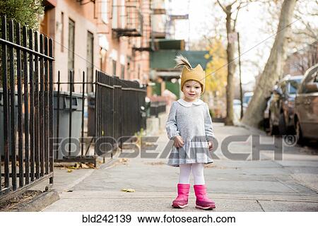 Stock Photo - Smiling Caucasian baby girl wearing crown hat on city sidewalk. Fotosearch