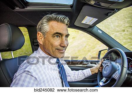 Stock Image - Smiling Caucasian businessman driving car. Fotosearch