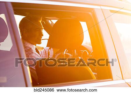 Stock Photograph - Smiling Caucasian businessman driving car on sunny day. Fotosearch