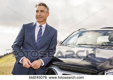 Stock Photo - Smiling Caucasian businessman leaning on car. Fotosearch