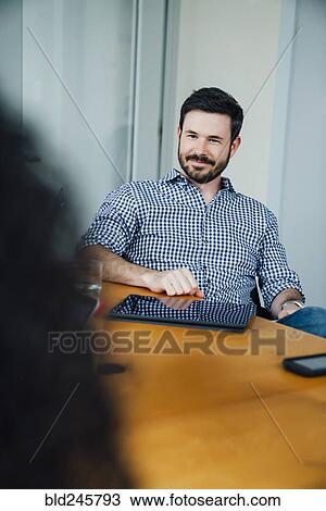 Stock Image - Smiling Caucasian businessman listening in meeting. Fotosearch