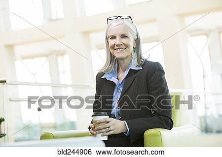 Stock Photograph - Smiling Caucasian businesswoman sitting in armchair drinking coffee. Fotosearch