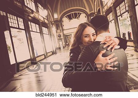 Stock Image - Smiling Caucasian couple hugging in lobby. Fotosearch